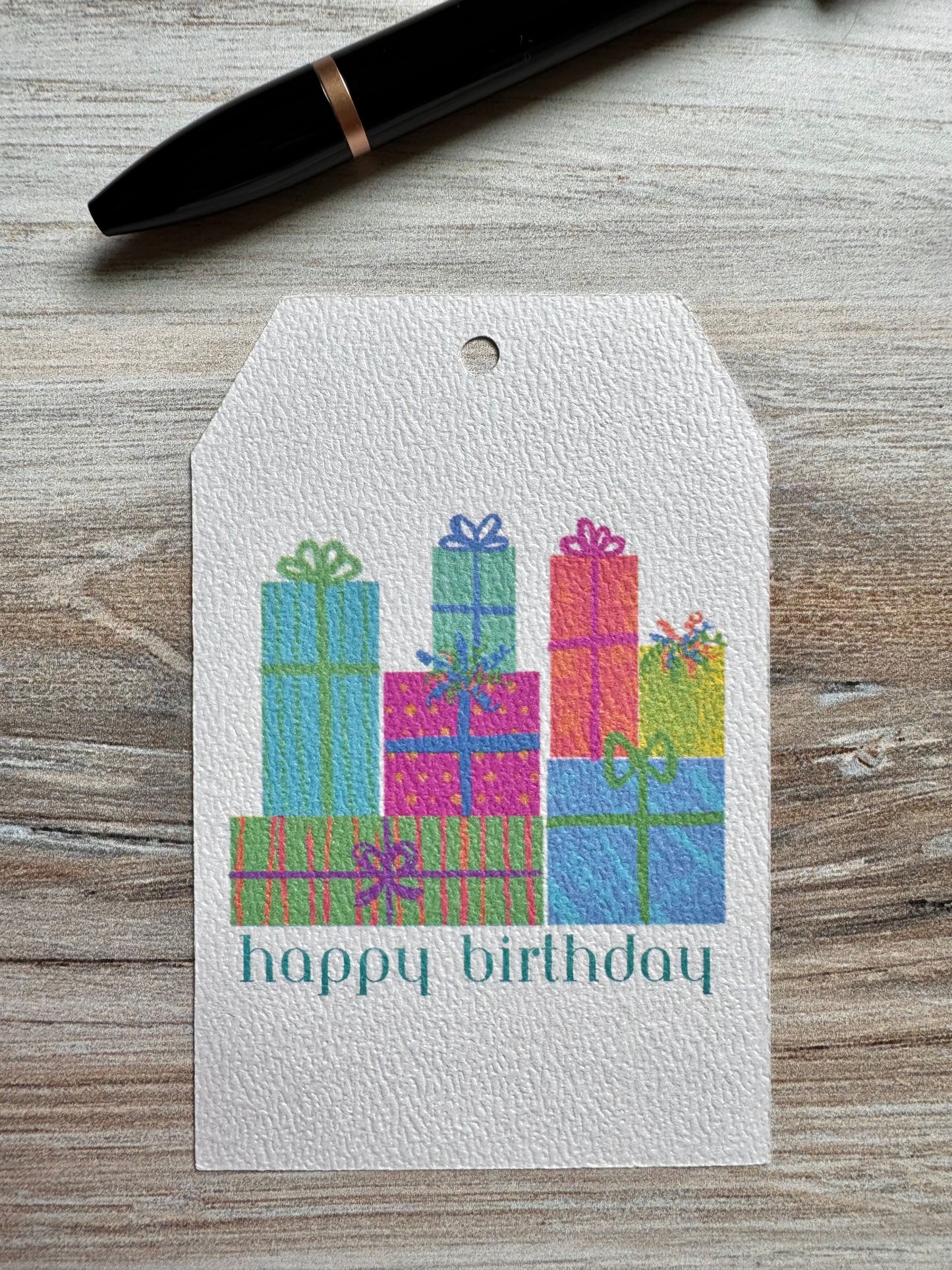 Gift tag with colorful presents and 'happy birthday' text on a wooden surface