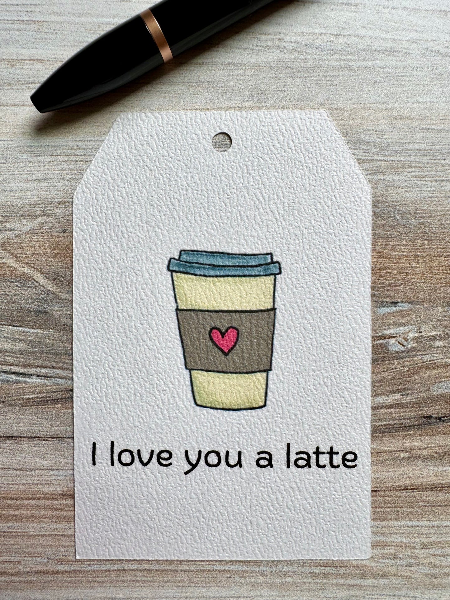 Gift Tag with a coffee cup illustration and 'I love you a latte' text placed on a wooden surface.