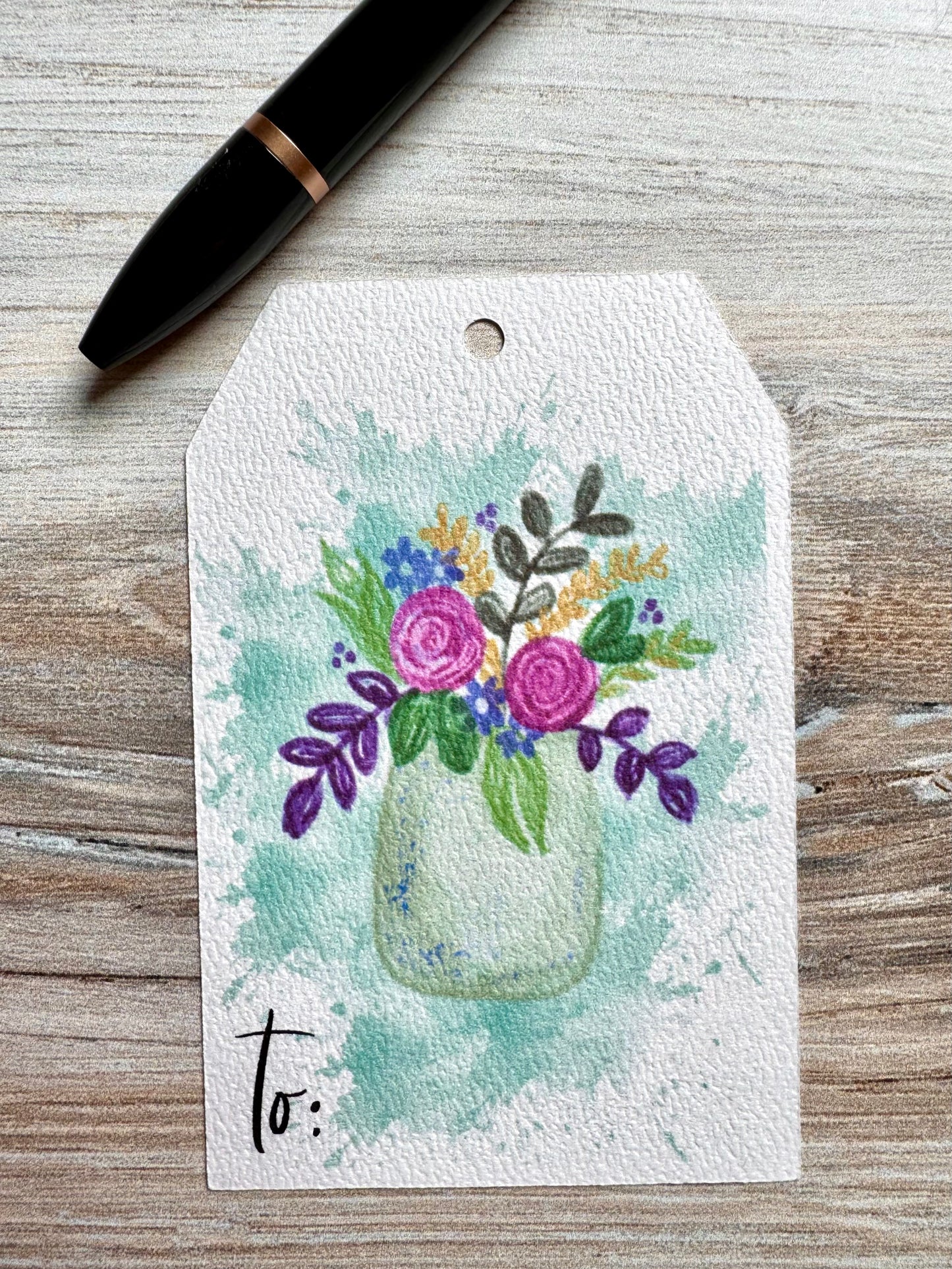 Gift tag with floral design and 'to' text on a wooden surface