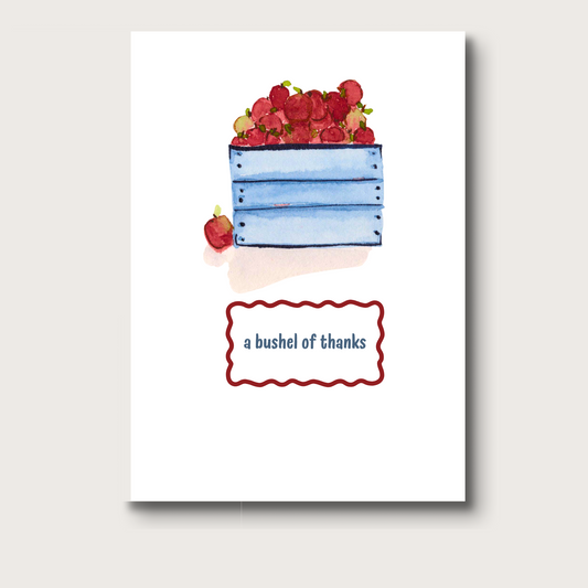 Card with watercolor illustration of a blue crate filled with red apples and a small apple on a white background. It reads "a bushel of thanks" below the image