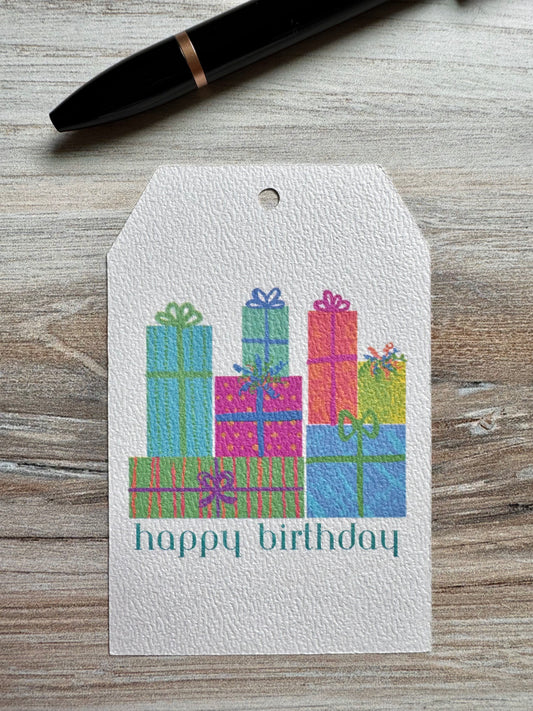 Gift tag with colorful presents and 'happy birthday' text on a wooden surface