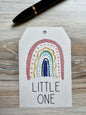Gift tag with minimalist rainbow design and 'LITTLE ONE' text placed on a wooden surface
