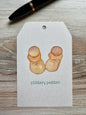Gift Tag with baby booties illustration and 'pitter, patter' text placed on a wooden surface with a pen.